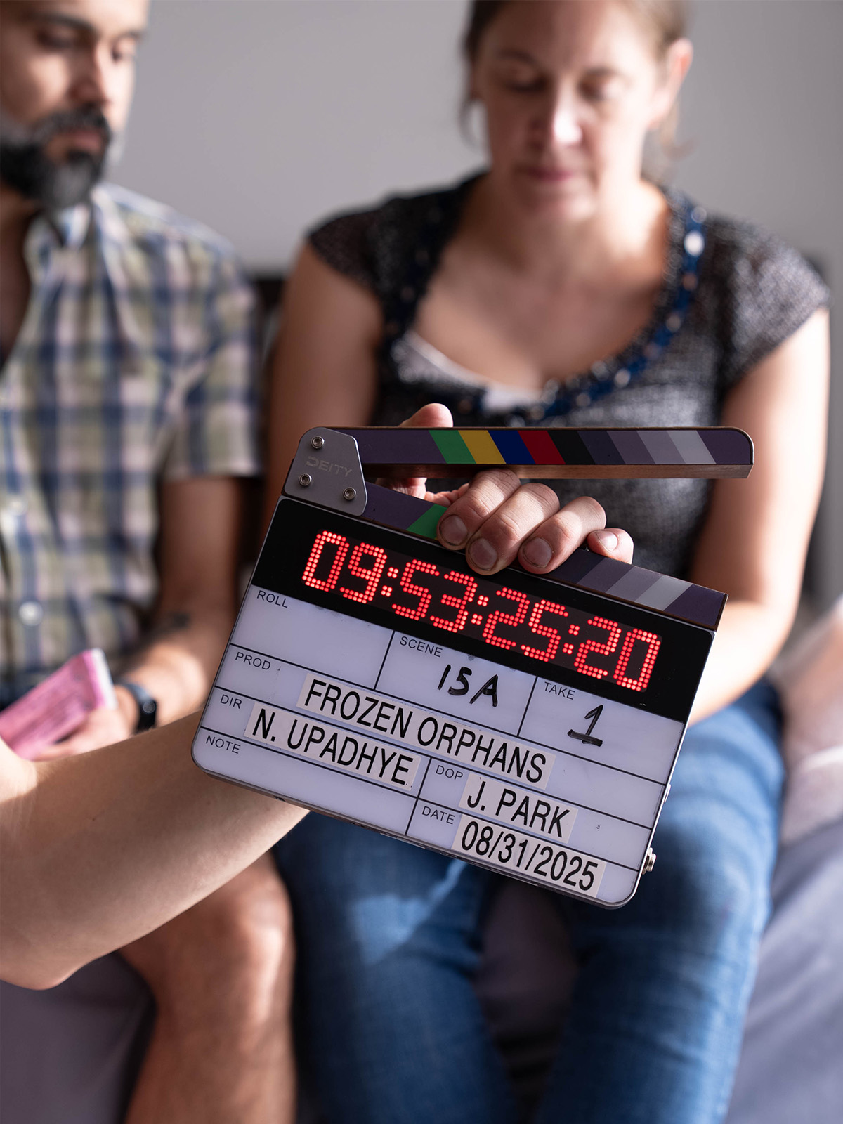 A filming clapper board for Frozen Orphans in front of two people